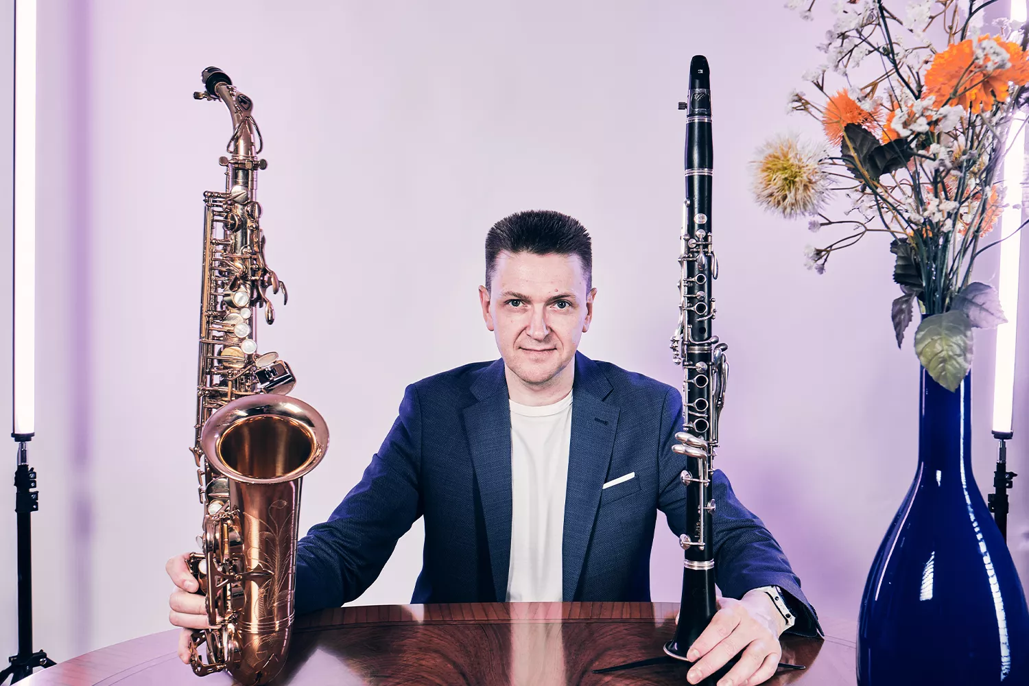 Viktor sitzend mit Klarinette in der Hand. Links eine Blumenvase mit Blumen, rechts en Saxophon, sowie eine weitere Vase mit Grünpflanzen