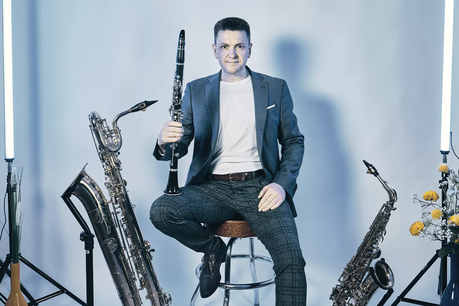 Viktor sitzt auf einem Hocker, Klarinette in der Hand, rechts und links stehen Saxophone