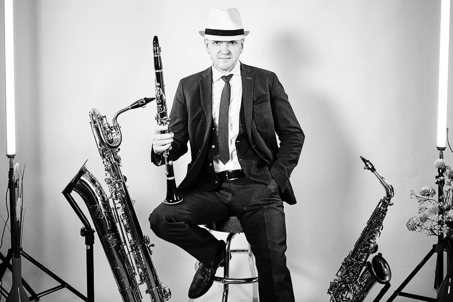 Viktor mit Hut sitzt auf einem Hocker, Klarinette in der Hand, rechts und links stehen Saxophone (schwarz/weiß-Bild)